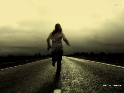 Poster for the Australian horror movie Wolf Creek: girl running away on road, filmed from behind